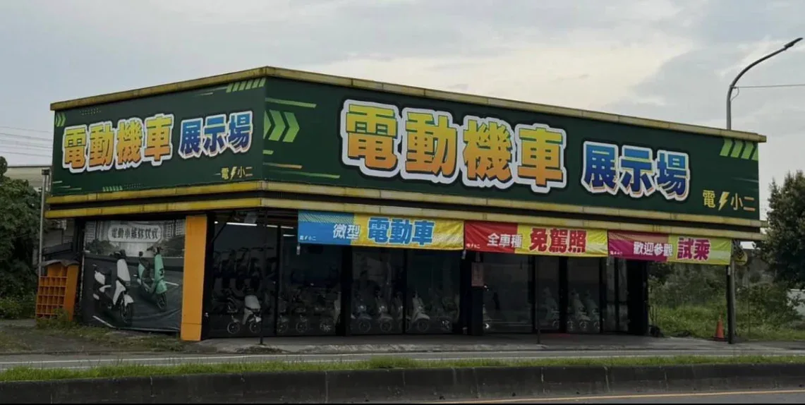 電小二冬山門市外觀：綠色招牌寫著電動機車展示場，玻璃窗內排列多台電動車